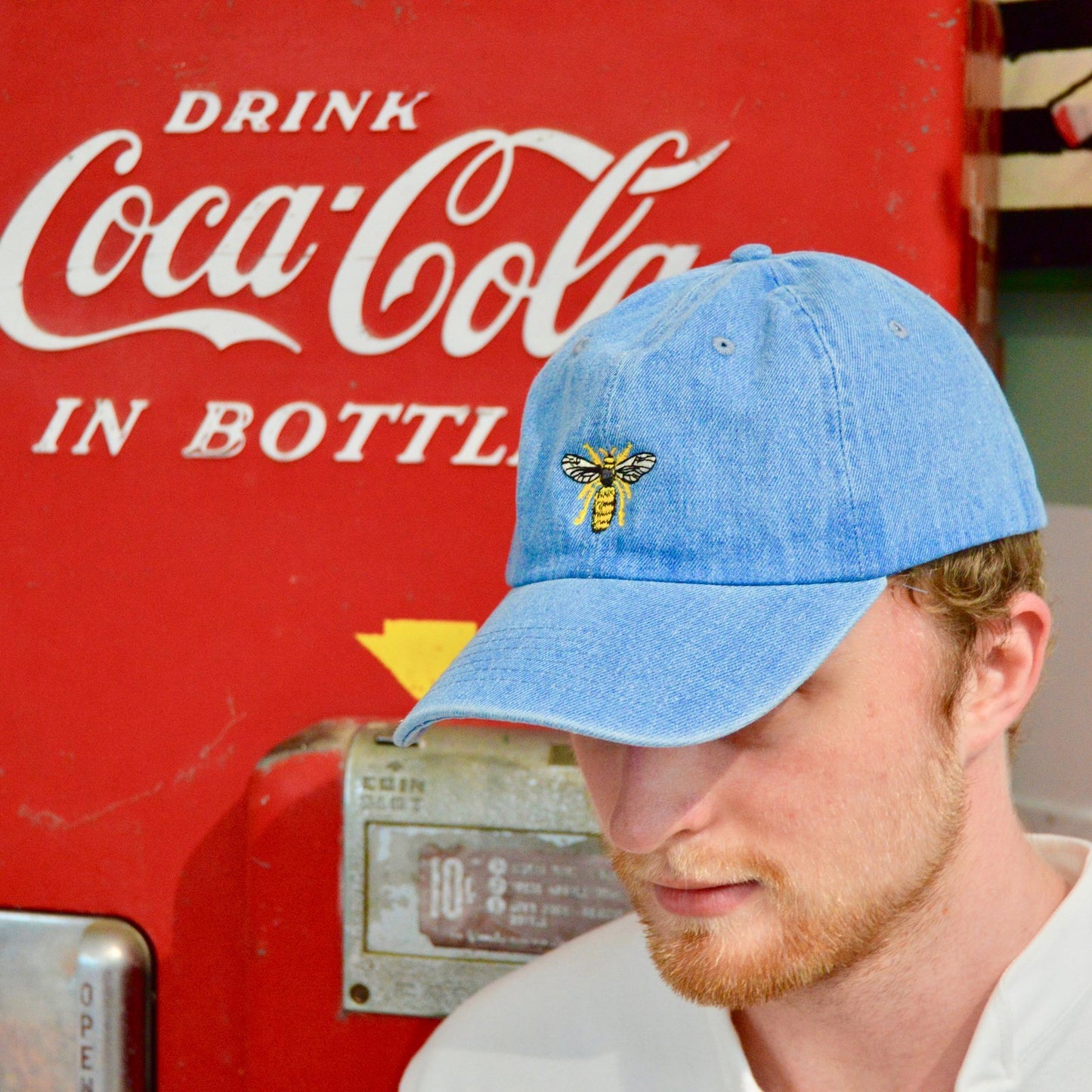 Male model wearing the Light Blue Drone Cap in front of a vintage Coca-Cola machine.
