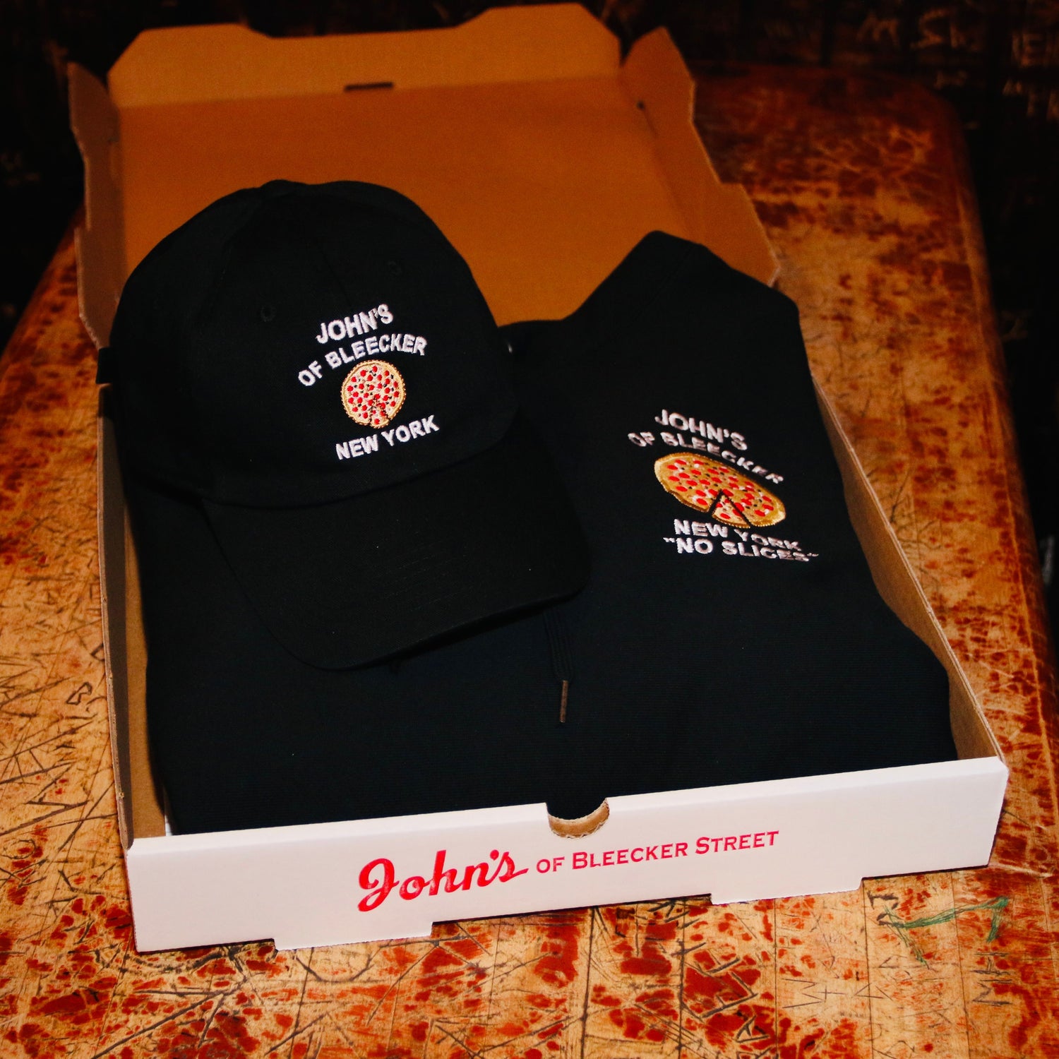 John's Pizza "No Slices" Hoodie and the John's Pizza "No Slices" Hat inside of a pizza box