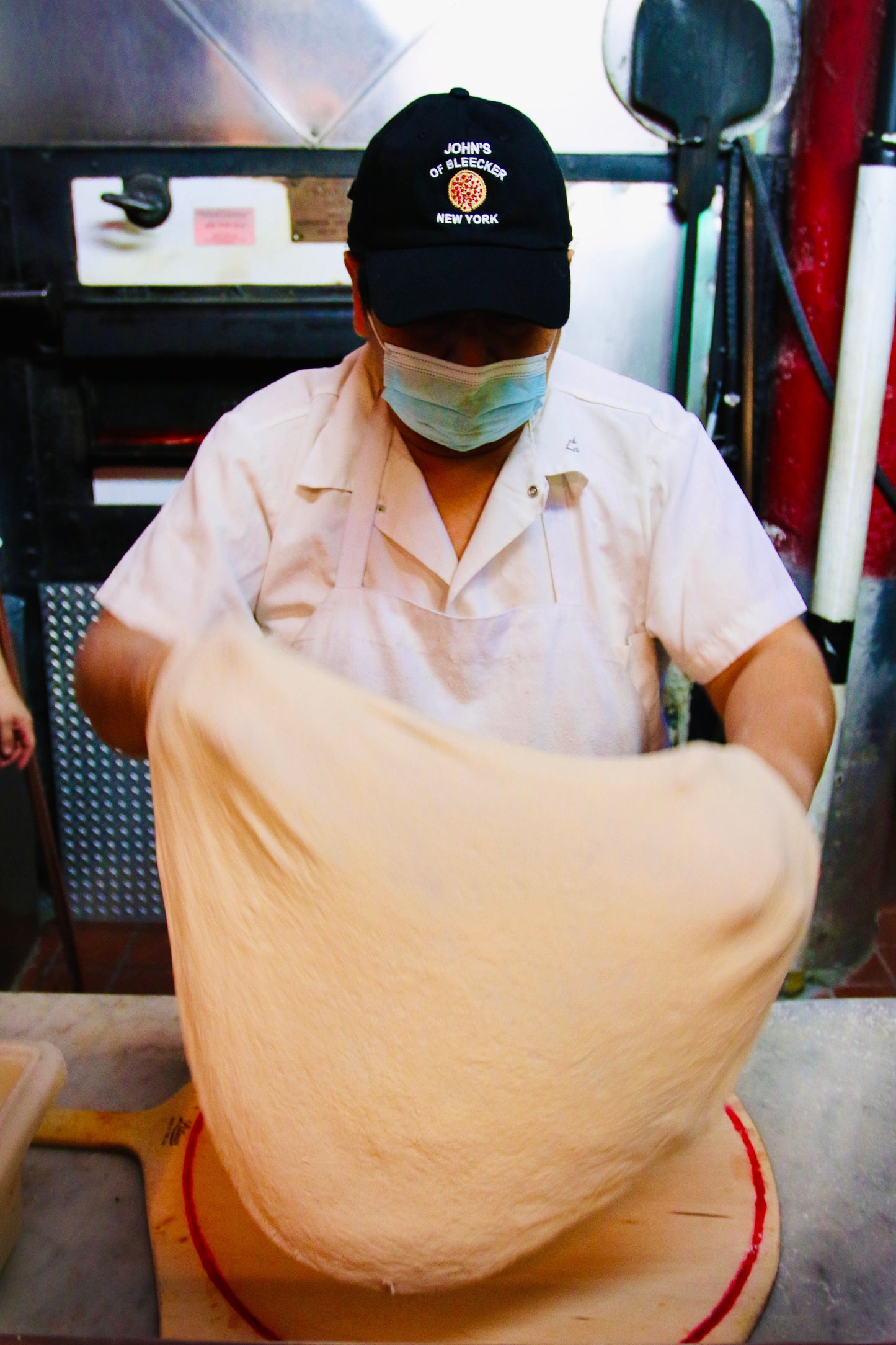 Man wearing the John's Pizza "No Slices" Hat  while making pizza dough